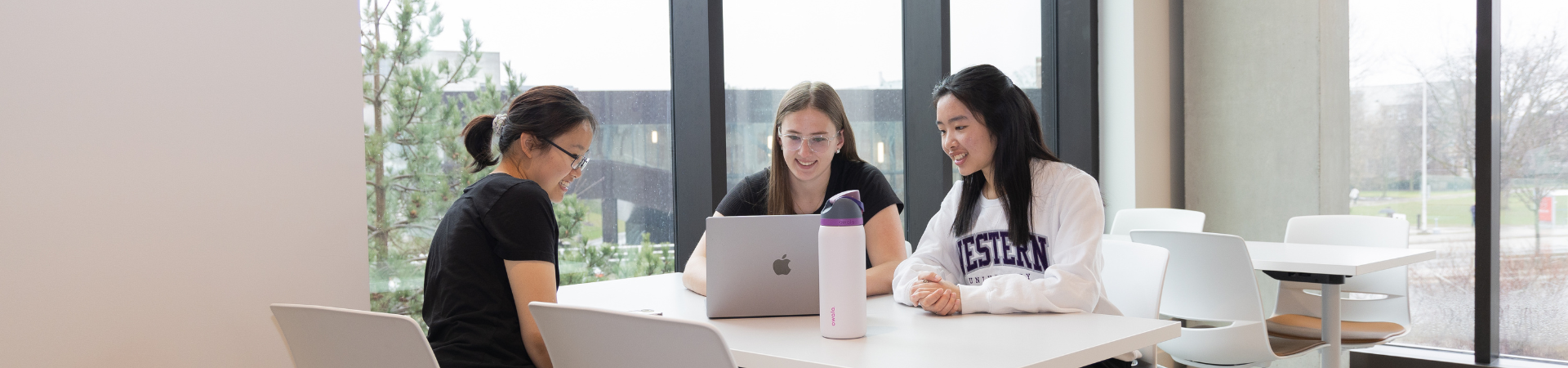 Three students work at a laptop together.