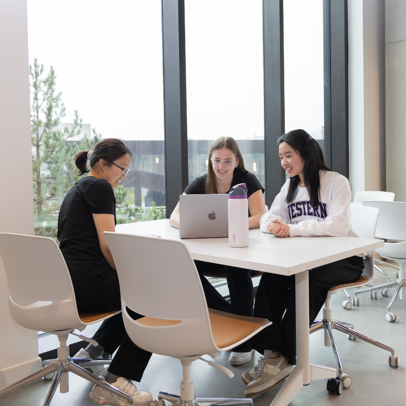 Three students work at a laptop together.
