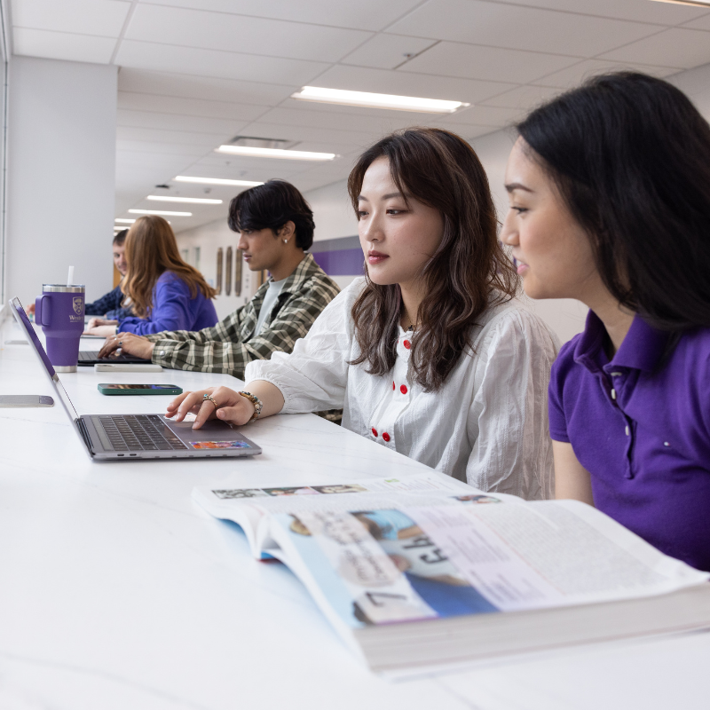 Two women work on writing materials, one on a computer, one with a notepad.