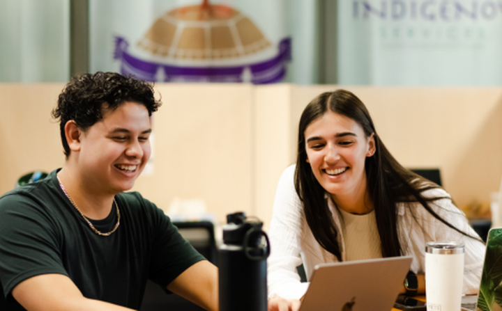 Two indigenous students work on laptops.